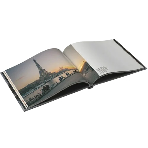 An open linen hardcover photo book, a full width travel photograph of a city at sunset across the left page and a smaller photograph with a caption on the right.